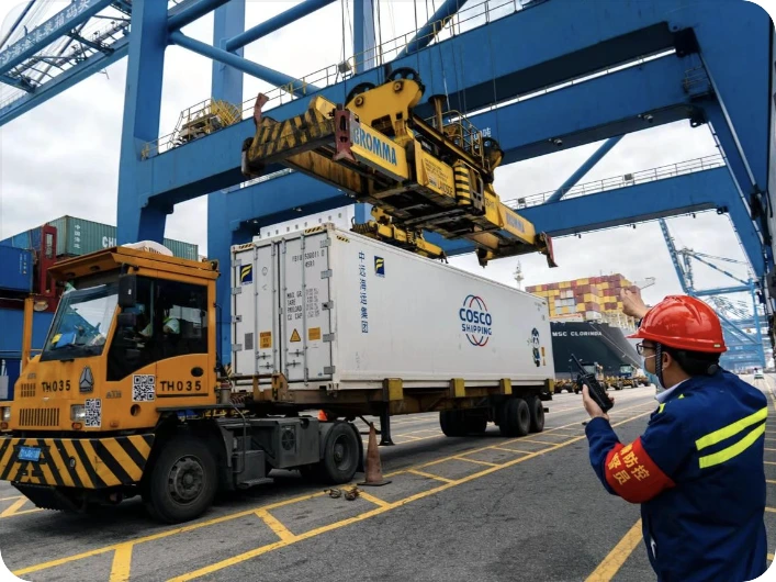 Refrigerated container being lifted at a terminal with a logistics worker overseeing handling — user-provided reference image.